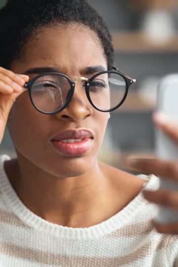Astigmatism. Young Black Female In Eyeglasses Trying To Read Message On Smartphone