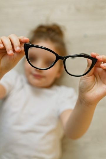 Child girl holding black-framed glasses in hands. Glasses in focus, child is blurred
