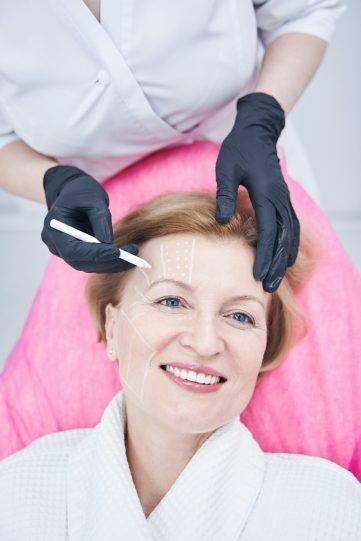 Beautician drawing marks on woman forehead in beauty salon